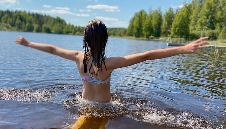 Flicka står i en sjö med armarna rakt ut, man ser henne bakifrån