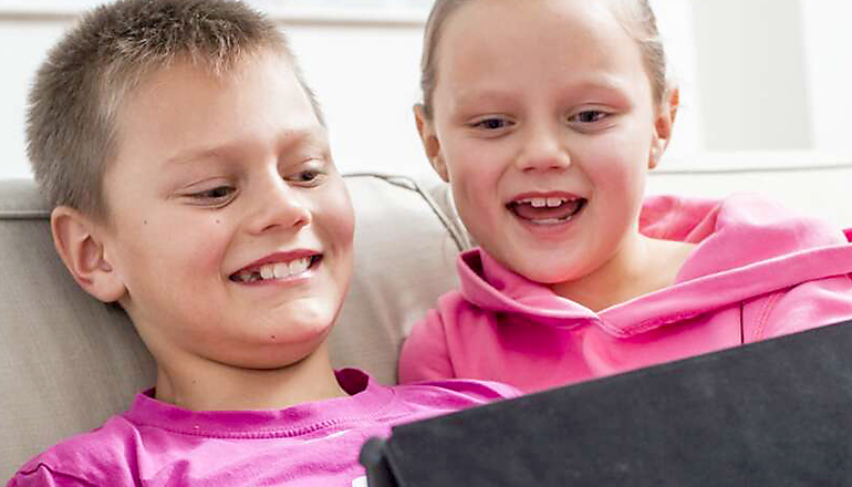 En pojke och en flicka tittar på en I-pad och skrattar