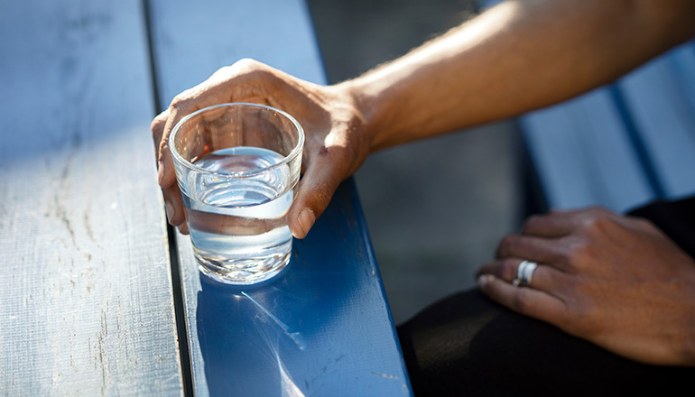 Bilden visar en hand som håller i ett glas med vatten