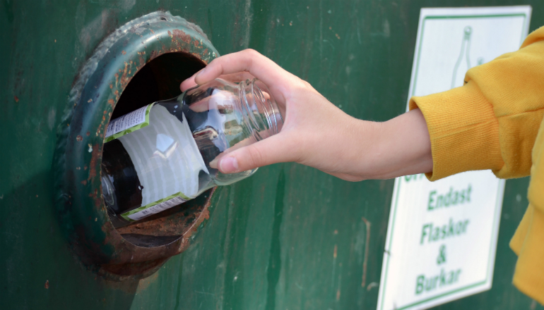 Hand som slänger ofärgat glas i en container på återvinningsstationen