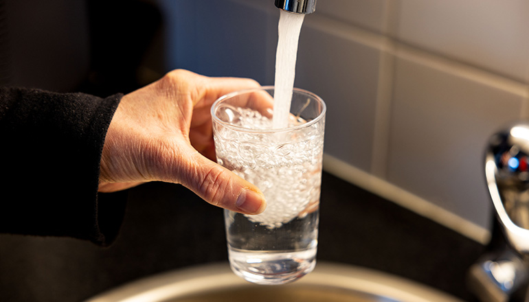 Bilden visar en hand som håller ett vattenglas under en kran med rinnande vatten