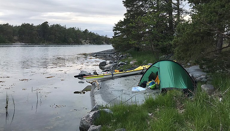 Bilden visar en kajak och ett tält intill vatten