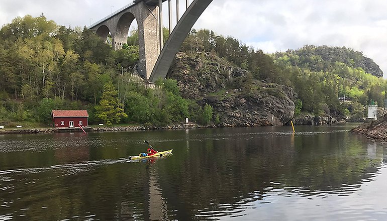 Bilden visar en människa som paddlar kajak under en hög bro