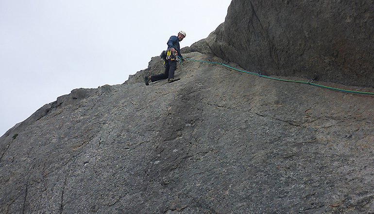 Bilden visar en man med klätterutrustning vid kanten på en bergvägg