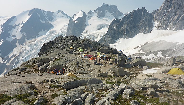Bilden visar fler tält upppställda intill varandra i ett bergsområde och i bakgrunden syns höga bergtoppar
